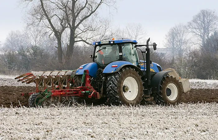 Blauer Traktor mit Pflug auf einem leicht verschneiten Acker.