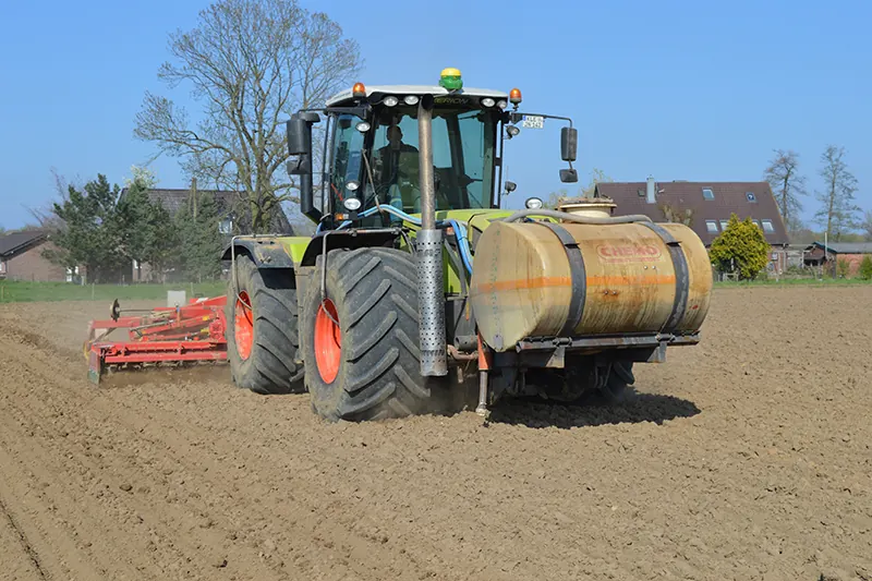 Traktor mit Fronttank und roter Kreiselegge auf einem vorbereiteten Acker.