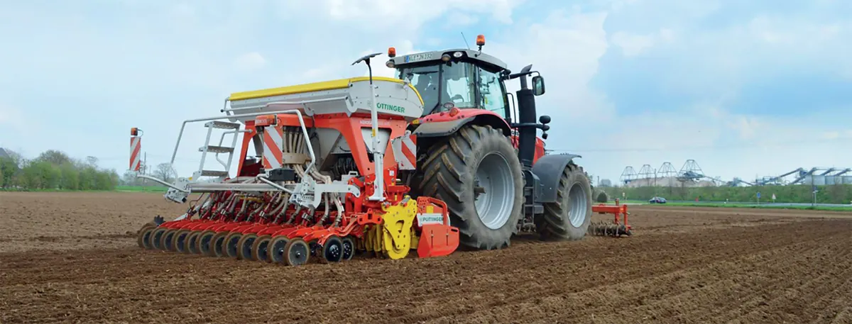 Roter Traktor mit Sämaschine auf einem frisch bearbeiteten Acker.