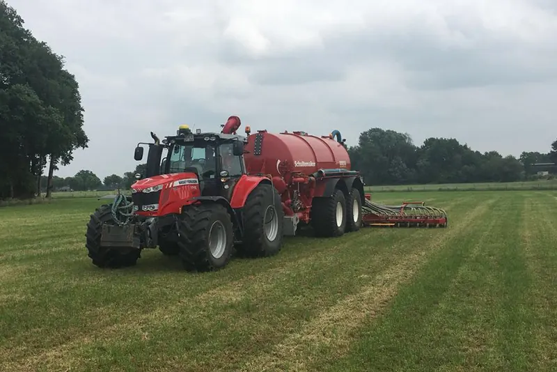 Roter Massey-Ferguson-Traktor mit rotem Güllefass und Ausbringgerät auf Grünland.